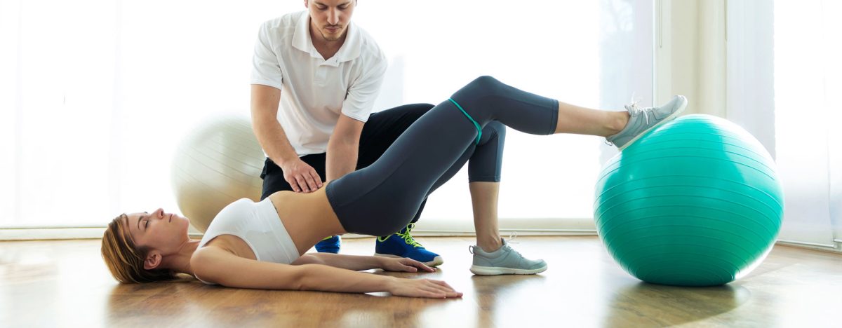 shot-physiotherapist-helping-patient-exercise-fitness-ball-physio-room